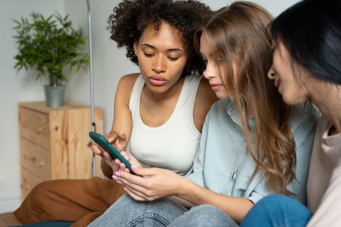 Three women sitting together looking at a phone, reflecting friendship of 10 years on the rocks and tension among friends.