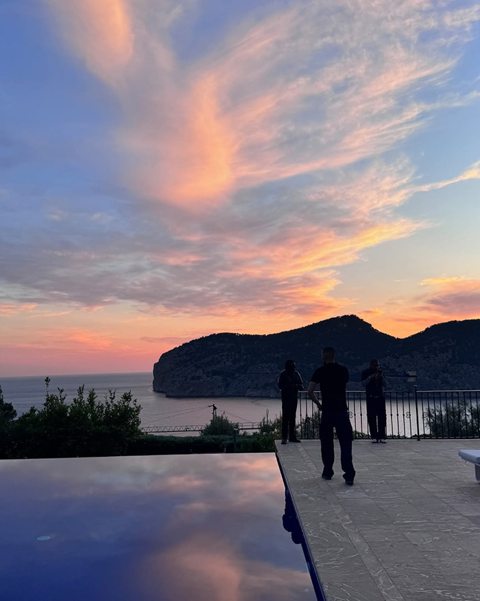 Sunset over coastal cliffs with three people standing near infinity pool, fans fear grooming related to Bianca Censori sister topic.