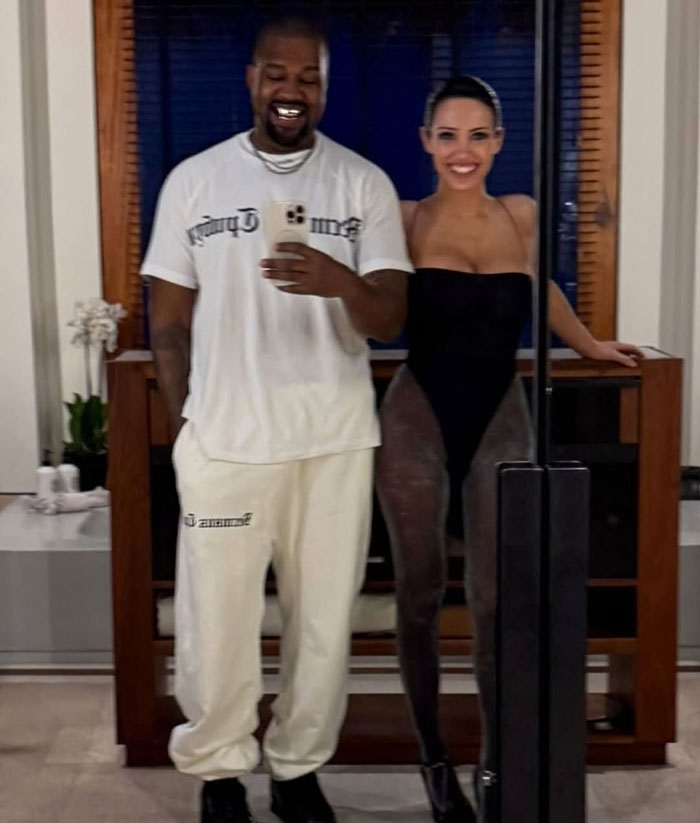 Bianca Censori posing in a daring bodysuit with hair extensions, sparking Kim K clone comments next to a man in casual wear.