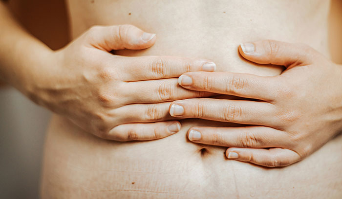 Close-up of hands pressing on the stomach showing common physical flaws of the human body in natural light.