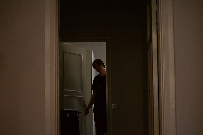 Person standing in a dimly lit doorway, illustrating isolation related to flaws of the human body.