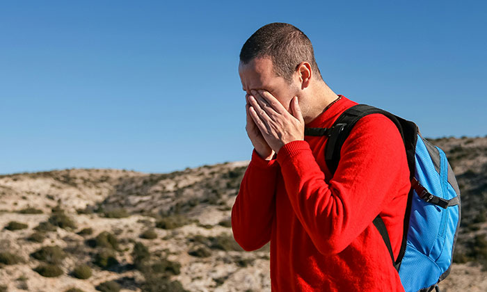 Man in red shirt outdoors covering his face, illustrating some of the biggest flaws of the human body in natural light.