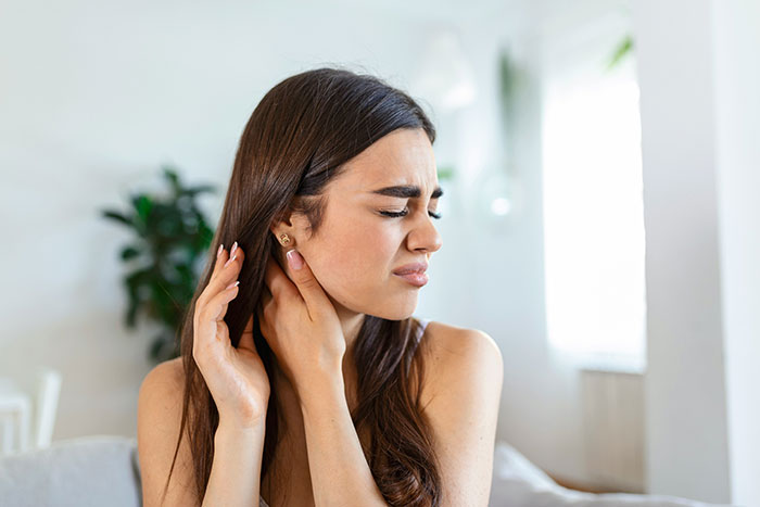 Young woman grimacing and holding her neck in pain, illustrating common flaws of the human body.
