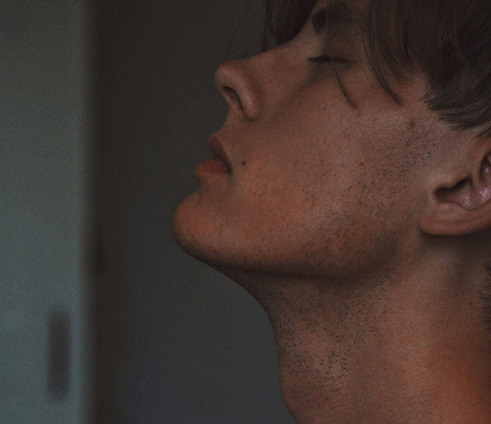 Close-up of a young man's face showing skin texture and natural flaws of the human body in soft lighting.