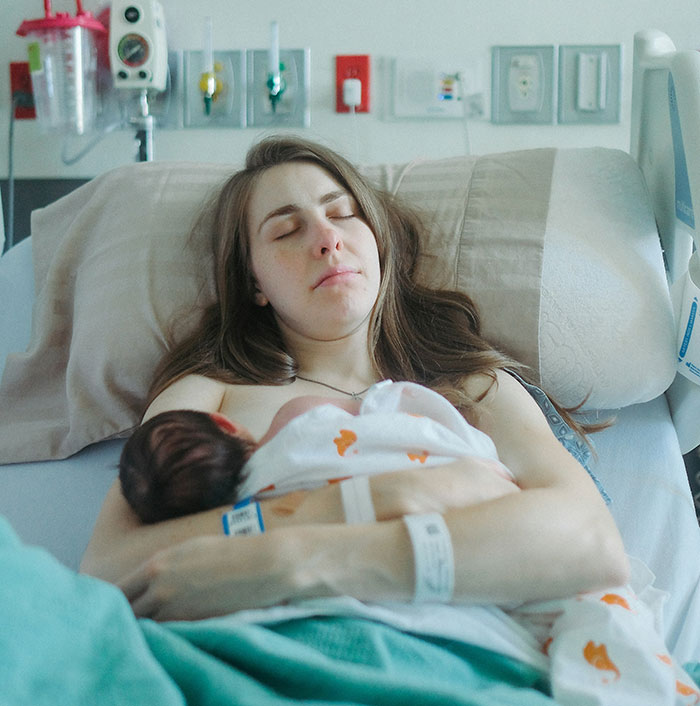 Mother resting in hospital bed holding newborn baby, highlighting the biggest flaws of the human body concept.