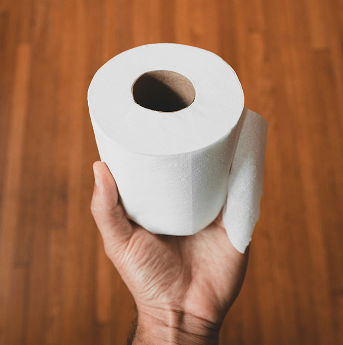 Hand holding a roll of toilet paper representing one of the biggest flaws of the human body related to hygiene and digestion.