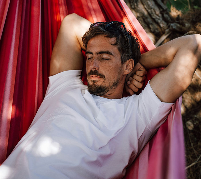Man resting in a hammock outdoors, highlighting common flaws of the human body in a natural setting.
