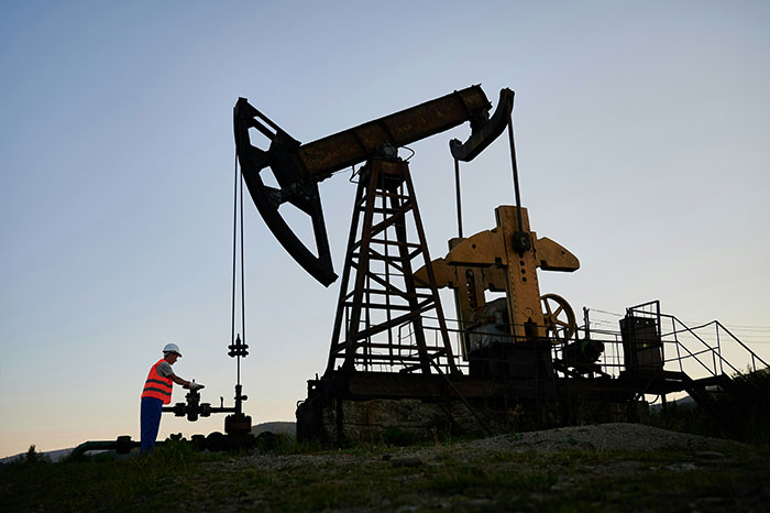 Worker inspecting oil rig at sunset, highlighting the biggest scandal in human history related to oil industry practices.