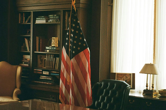 Office with American flag, leather chair, wooden bookshelf, and soft natural light highlighting biggest scandal in human history theme.