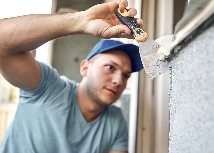Man in a blue cap applying plaster on wall during kitchen renovation, representing revenge and renovation themes.