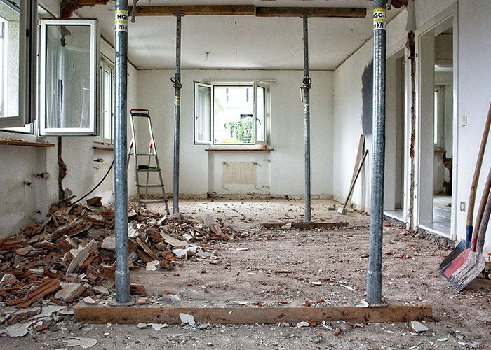Kitchen renovation in progress with exposed beams, construction debris, and tools inside an empty room.