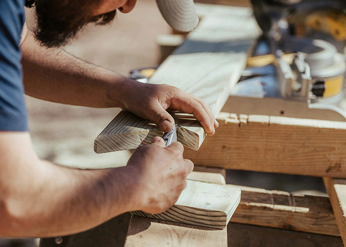 Man working on kitchen renovation, shaping a wooden board with a hand tool in a bright workshop setting.