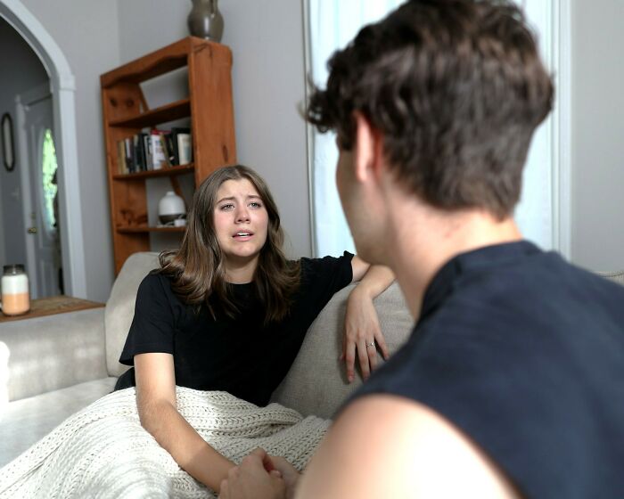 Woman explaining twins pregnancy duration to a man while sitting on a couch covered with a blanket in a living room.
