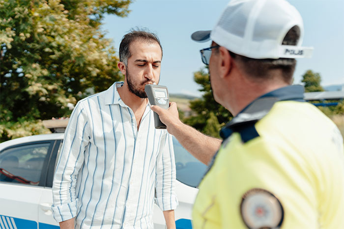 Man in striped shirt blowing into breathalyzer held by police officer during roadside garage blocking incident