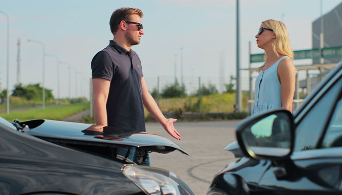 Man and woman argue next to two cars, illustrating a guy blocking garage and swearing at woman&rsquo;s family incident.
