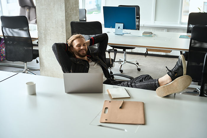 Man relaxing at office desk with laptop, showing minimal work time after commute and break, avoiding overtime hours. Man relaxing at office desk with laptop, showing minimal work time after commute and break, avoiding overtime hours.