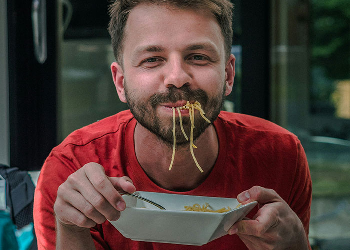 Man in a red shirt eating noodles during lunch break, illustrating boss demands and workplace sacrifices concept. Man in a red shirt eating noodles during lunch break, illustrating boss demands and workplace sacrifices concept.