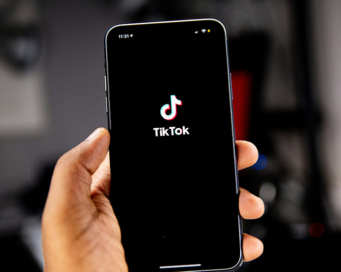 Hand holding smartphone displaying TikTok app, related to viral scarf challenge involving boy aged 12 safety concerns.