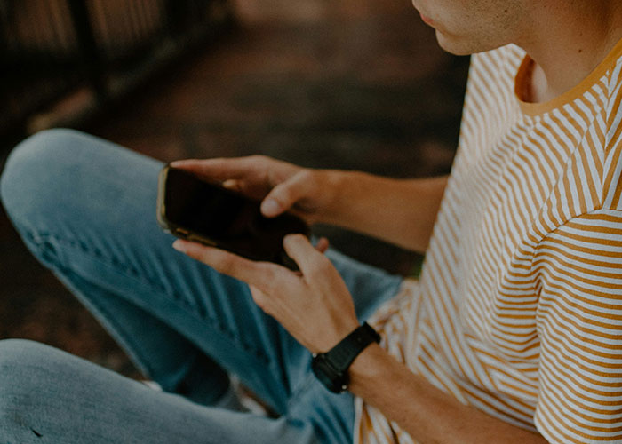 Man in a striped shirt holding phone, appearing concerned, relating to guy finding old photo and micro-cheating accusation.