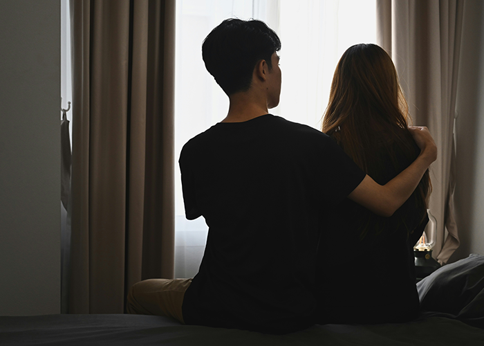 Couple sitting on bed with man holding woman, reflecting tension over guy finding old photo and micro-cheating accusation.
