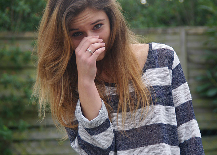 Young woman in striped sweater covering her face, symbolizing discomfort related to micro-cheating accusations.