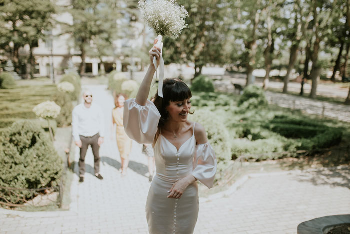 Bride holding a bouquet outdoors smiling with guests in the background during a wedding celebration. Bride holding a bouquet outdoors smiling with guests in the background during a wedding celebration.