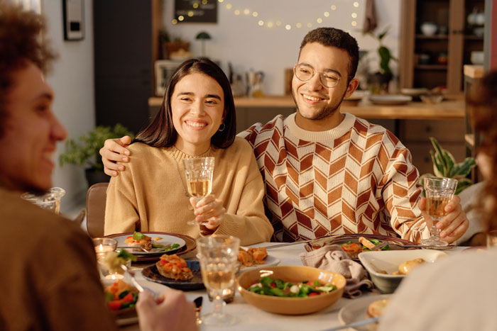 Young woman with boyfriend at dinner, smiling nervously while meeting boyfriend&rsquo;s mom and facing subtle comparisons.