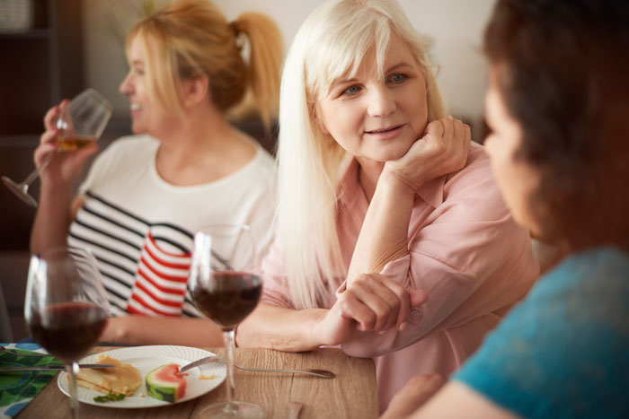 Middle-aged woman listening intently while another woman drinks wine, highlighting conflict with boyfriend&rsquo;s mom and comparisons.