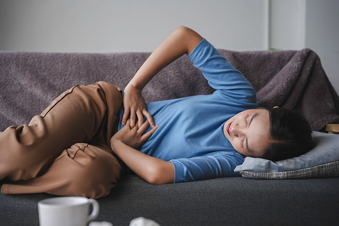 Woman lying on couch holding stomach in discomfort after being fed slugs and pet snail by boyfriend for months