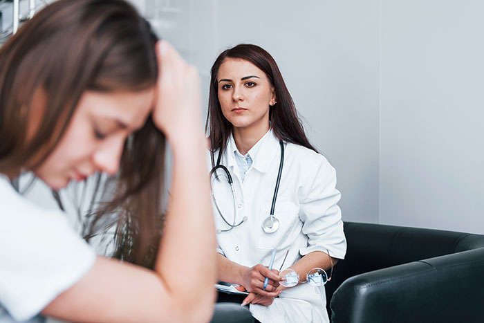 Woman troubled and stressed while a female doctor with stethoscope listens carefully during a consultation session.