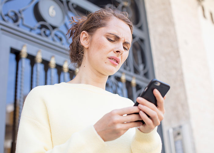 Upset woman outside looking at phone, frustrated about friend&rsquo;s girlfriend not allowing them to sleep in the same bed.