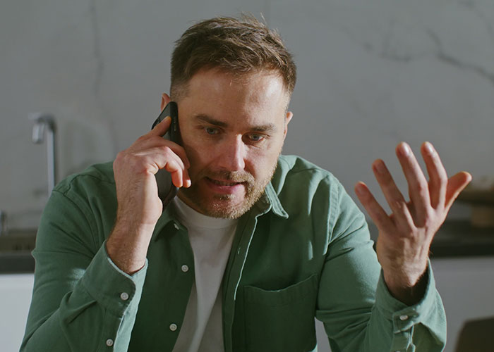 Man in green shirt looking upset while talking on phone, expressing frustration about friend&rsquo;s girlfriend and bed situation.