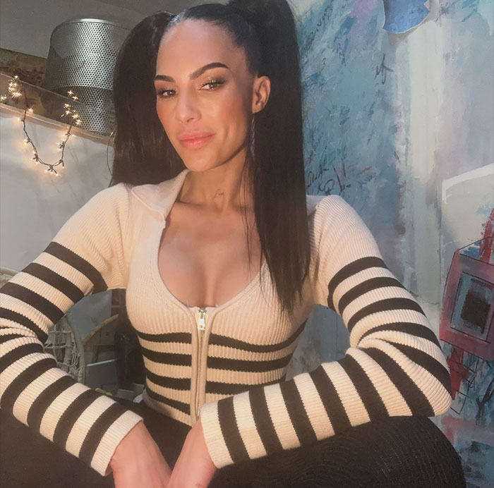 Amanza Smith posing confidently indoors wearing a striped zip-up sweater highlighting Selling Sunset net worth rankings.