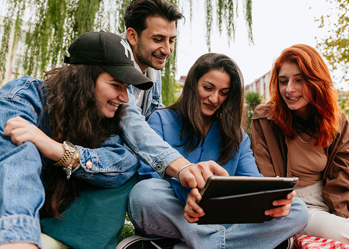 A group of friends smiling and looking at a tablet together, illustrating moments of breaking guy or girl code.