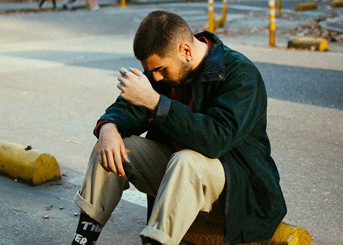Man sitting on a curb in casual clothing, reflecting thoughtfully, illustrating moments when people broke guy or girl code.