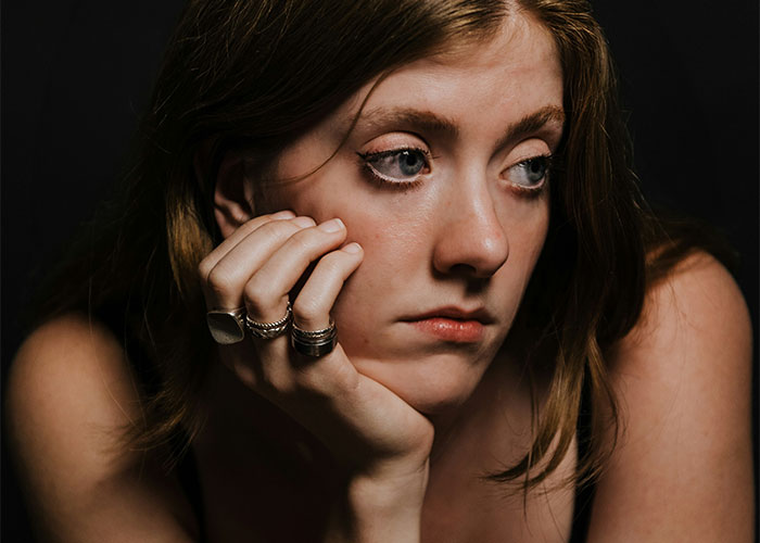 Young woman with rings on her fingers resting her face on her hand, showing a contemplative mood breaking girl code.