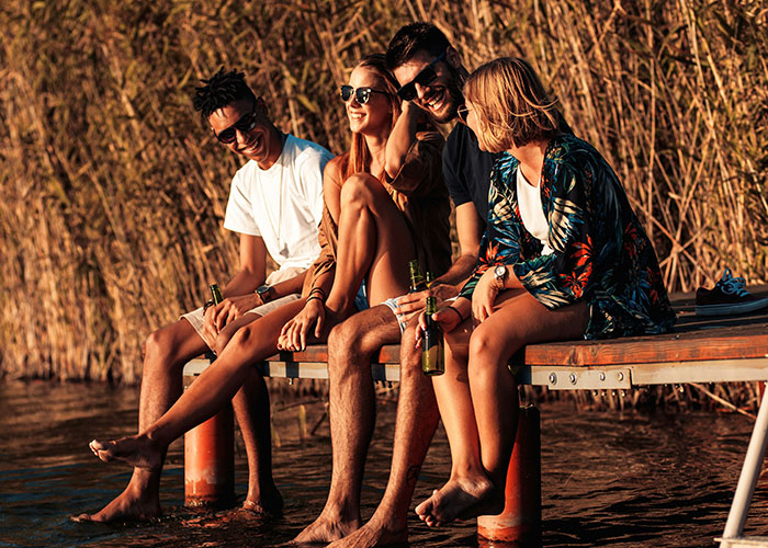 Four friends smiling and relaxing on a dock at sunset, illustrating moments when people broke guy or girl code for a better choice.