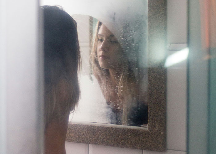 Young woman looking at her reflection in a foggy mirror illustrating moments people broke guy or girl code choices.