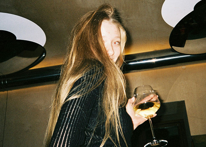 Young woman with long hair holding a glass of white wine, breaking guy or girl code in a social setting.