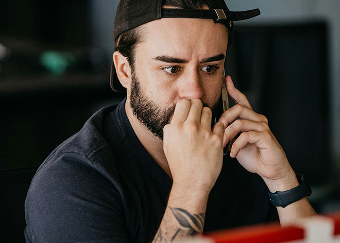 Bearded man in a cap making a serious phone call, illustrating moments when people broke guy or girl code.