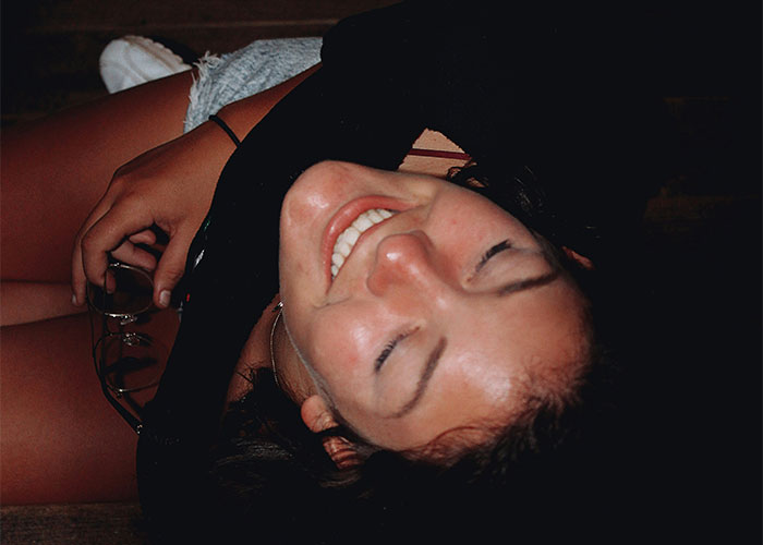 Smiling woman lying down with eyes closed, holding glasses, representing moments people broke guy or girl code.