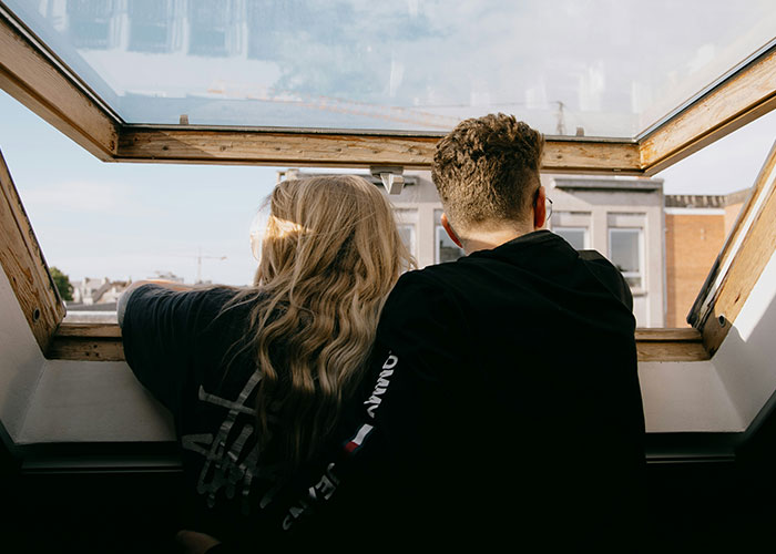 Couple looking out of an open attic window, illustrating moments when people broke guy or girl code for better choices.