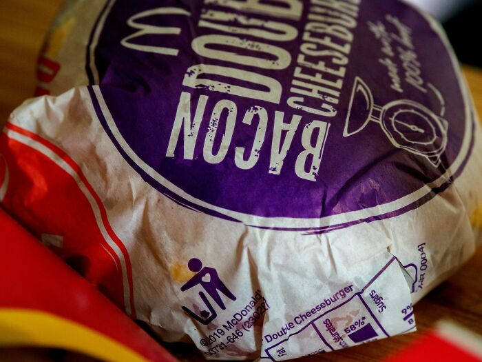 Close-up of a wrapped double cheeseburger with bacon, highlighting packaging details and texture of abandoned explorers' discovery.