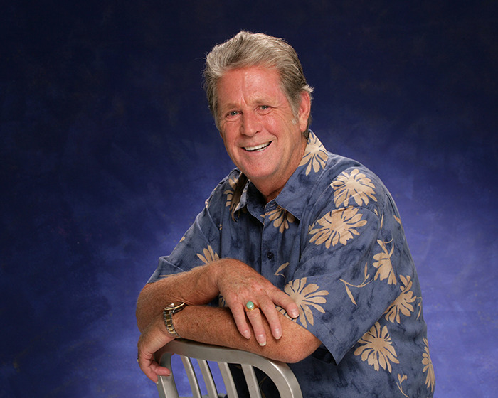 Smiling man in a floral shirt leaning on a chair, representing the Beach Boys legendary co-founder and musical genius.