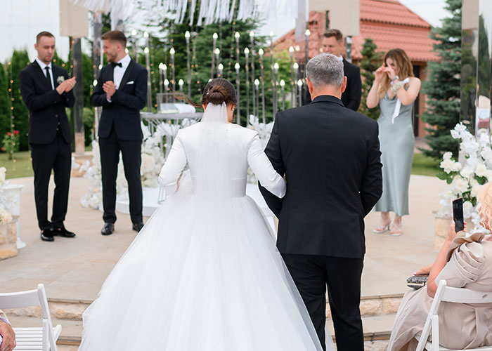 Bride walking down the aisle with her dad at an outdoor wedding ceremony, capturing wedding drama and family tension moments.