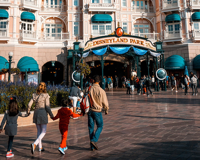 Family walking towards entrance of Disneyland Park on a sunny day with crowds gathered at the entrance.