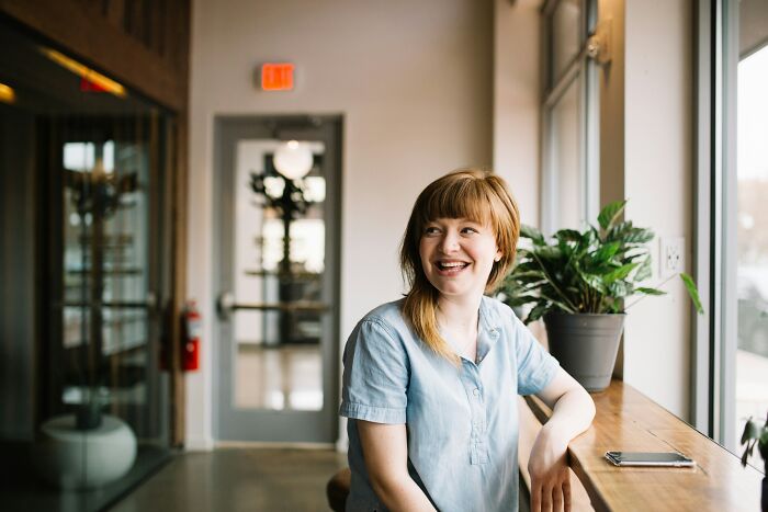 Young woman sitting by a window in a bright room, smiling and relaxing, illustrating casual habits that may cause long-term damage.