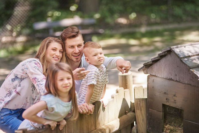 Family gathering outside near a wooden fence with a man, woman, and two children enjoying time together.