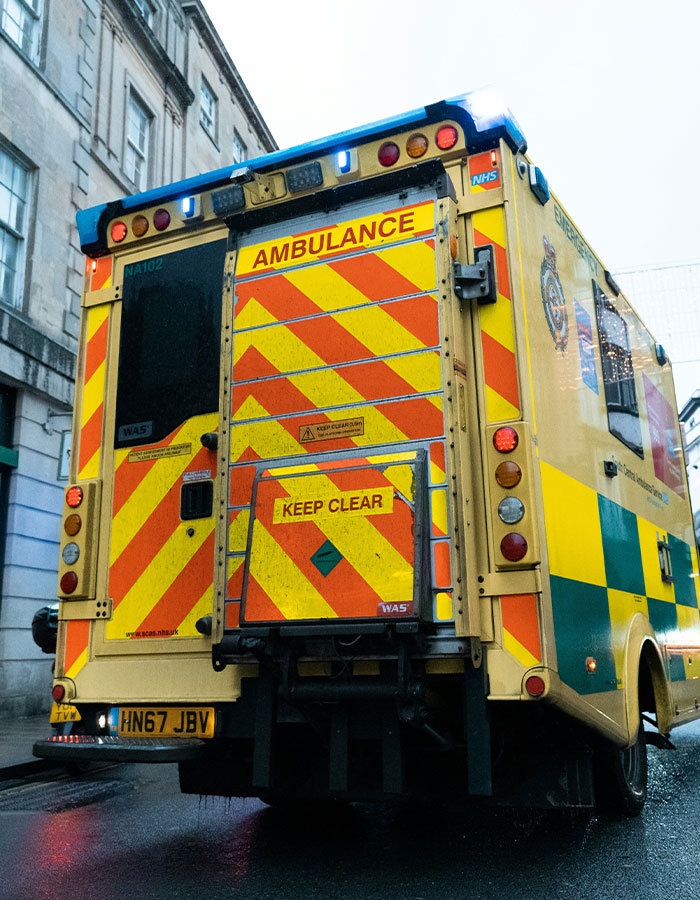 Yellow and green ambulance with flashing lights on a city street, related to excessive caffeine consumption incidents.
