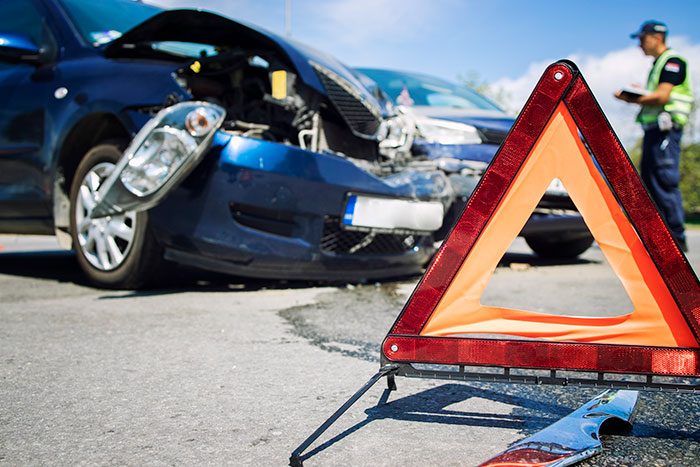 Warning triangle on road near damaged car after major accident with emergency responder taking notes nearby Warning triangle on road near damaged car after major accident with emergency responder taking notes nearby